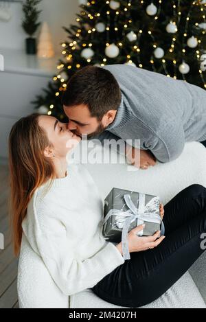 coppia felice vicino a scatole regalo e albero di natale. coppia abbracciandosi e guardandosi vicino all'albero di natale. Foto Stock
