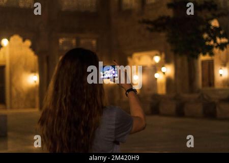 Una giovane donna cammina lungo la stretta strada del villaggio arabo e scatta foto con il suo telefono Foto Stock