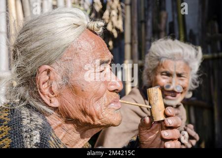 Ritratto di un vecchio Apatani indossando il tradizionale acconciatura con la maglia alla fronte, fumo tubo Foto Stock