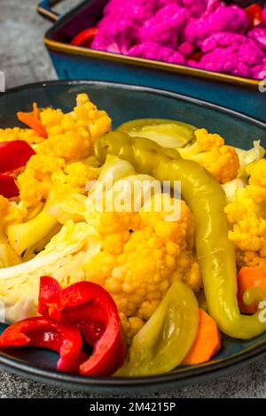 Sottaceti fatti in casa con cavolfiore giallo e viola in un piatto su sfondo grigio Foto Stock