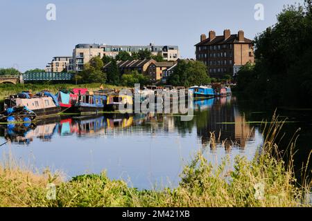 Una scena cittadina nella parte est di Londra in un caldo e muggy giorno di luglio, lungo il fiume Lea, dove le barche ormeggiate casa contrasto con gli edifici di appartamenti. Vita a Londra. Foto Stock