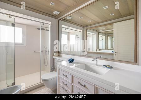 Bagno lussuoso con un grande specchio con un'insolita riflessione multipla. Ampia zona doccia con ringhiera in vetro. Luce solare intensa di giorno Foto Stock