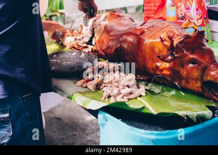 Macellaio affettare a pezzi il preferito di tutti i tempi, il popolare delizioso arrosto di maiale intero croccante o Lechon Baboy posato sulla foglia di banana sul tavolo Foto Stock