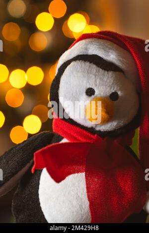 Primo piano di un pinguino di lusso di Natale vestito con un cappello di Babbo Natale e sciarpa rossa con luci bokeh dietro. Foto Stock