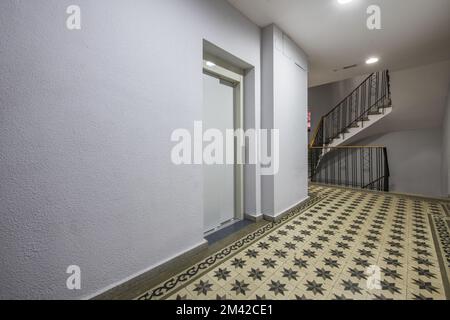 Atterraggio di un edificio residenziale urbano con scale con ringhiere in ferro battuto, pavimenti idraulici piastrellati e un ascensore con porte in metallo leggero Foto Stock