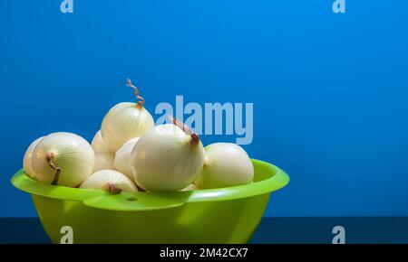 Cipolle pelate in un colino di plastica verde. Spazio di copia. Sfondo blu Foto Stock