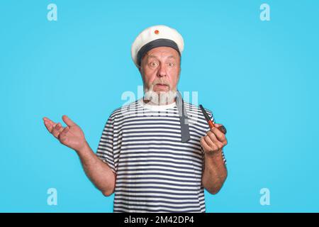 Non lo so. Un vecchio marinaio con uno sguardo confuso. Tubo fumante, uniforme marina. su uno sfondo blu isolato Foto Stock