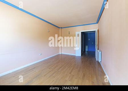 Soggiorno vuoto con pareti e soffitto color pesca chiaro, cornici in gesso blu e pavimento in legno Foto Stock