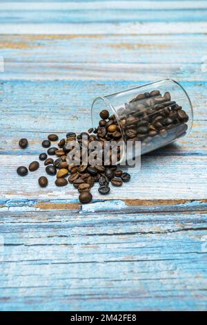 Vaso di vetro capovolto su alcune tavole blu piene di chicchi di caffè tostati Foto Stock