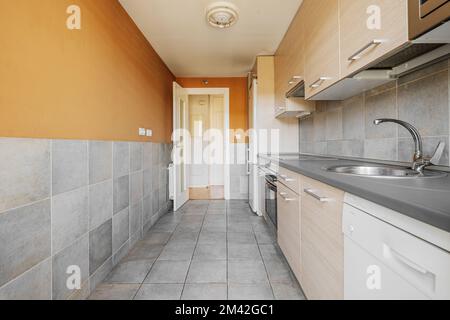 cucina con armadi in legno chiaro con ripiani grigi, elettrodomestici bianchi e piastrelle quadrate su pareti e pavimenti Foto Stock