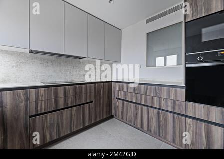 Cucina recentemente installata in design contemporaneo con armadi in legno di radice, elettrodomestici neri lucidi e pavimenti in piastrelle grigie. Foto Stock