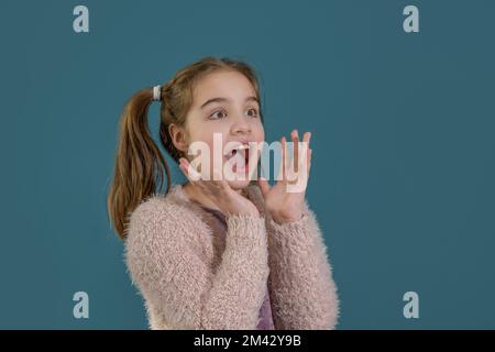 Le migliori notizie! Primo piano ritratto di bella, carina, ragazza adolescente in maglione rosa con bocca aperta e grandi occhi isolati su sfondo blu Foto Stock