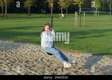 Divertimento autunnale all'aperto. Giovane ragazza in sella a un bungee appeso sul parco giochi Foto Stock