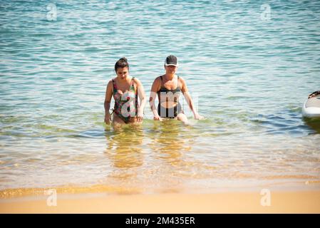 Madre e figlia, in bikini, stanno uscendo dall'acqua alla spiaggia di Porto da barra a Salvador, Bahia. Foto Stock