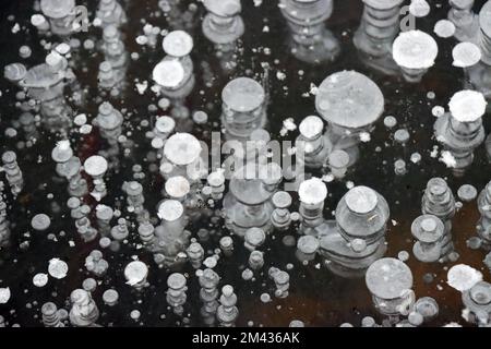 Im EIS eines Teichs eingefrorene Luftblasen bilden ein abraktes Muster Foto Stock