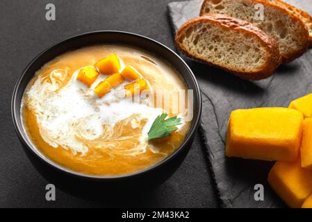 Zuppa tradizionale di zucca con consistenza cremosa e setosa. Pane e ingredienti per la zuppa l'uno accanto all'altro Foto Stock