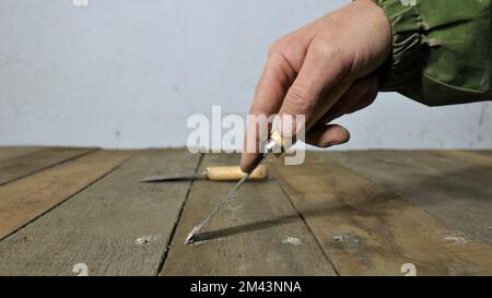 una mano con una spatola stretta copre con piccoli fori di mastice da un chiodo martellato in legno, cosparso di una soluzione di crepe e fori Foto Stock