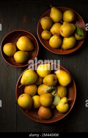 Deliziose e succose pere fatte in casa in piatti di argilla su sfondo scuro in stile rustico. Foto Stock