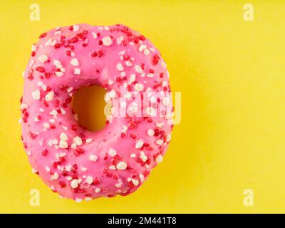 Ciambella rosa dolce con spolverini multicolore su fondo giallo. Dessert dolce colorato Foto Stock