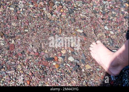 Punte a piedi nudi nelle rocce multicolore di Rainbow nel torrente delle valanghe che conducono verso il lago McDonald al Glacier National Park, Montana, USA Foto Stock