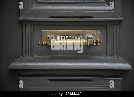 Antica casa neoclassica porta d'ingresso in legno grigio con una antica fessura in ottone con lettere greche a Nafplio, Grecia. Foto Stock