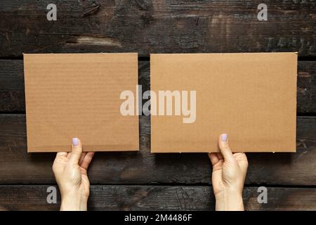 Le mani femminili tengono due carte di cartone in mano su uno sfondo di legno, spazio per il testo Foto Stock