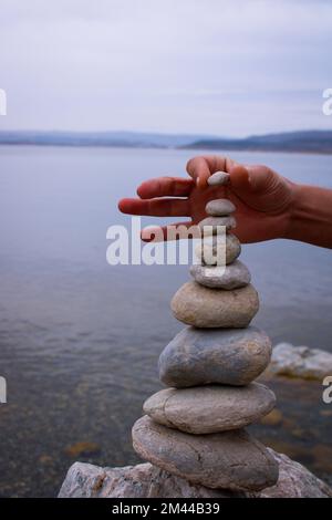 Una mano costruisce l'equilibrio sui ciottoli. Equilibrio perfetto tra la pila di ciottoli sulla riva del mare. Concetto di equilibrio, armonia e meditazione Foto Stock