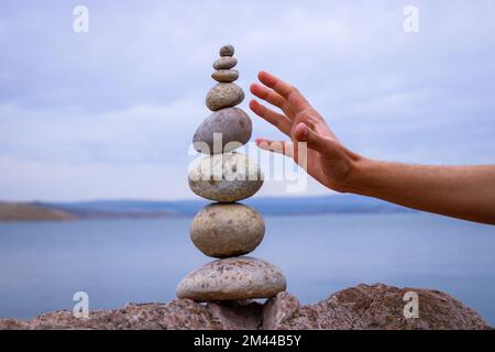 Una mano costruisce l'equilibrio sui ciottoli. Equilibrio perfetto tra la pila di ciottoli sulla riva del mare. Concetto di equilibrio, armonia e meditazione. Foto Stock