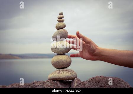 Una mano costruisce l'equilibrio sui ciottoli. Equilibrio perfetto tra la pila di ciottoli sulla riva del mare. Concetto di equilibrio, armonia e meditazione. Foto Stock