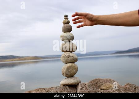 Una mano costruisce l'equilibrio sui ciottoli. Equilibrio perfetto tra la pila di ciottoli sulla riva del mare. Concetto di equilibrio, armonia e meditazione. Foto Stock