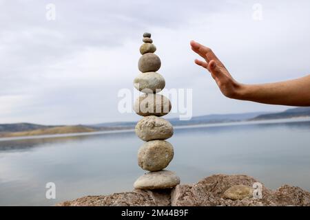 Una mano costruisce l'equilibrio sui ciottoli. Equilibrio perfetto tra la pila di ciottoli sulla riva del mare. Concetto di equilibrio, armonia e meditazione. Foto Stock