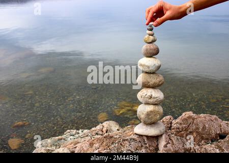 Una mano costruisce l'equilibrio sui ciottoli. Equilibrio perfetto tra la pila di ciottoli sulla riva del mare. Concetto di equilibrio, armonia e meditazione. Foto Stock