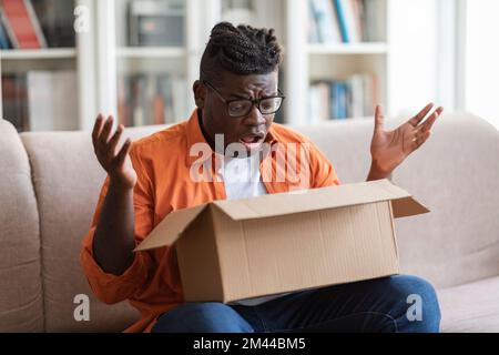 Scioccato afro americano giovane ragazzo cliente di apertura pacco Foto Stock