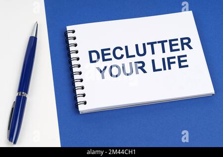 Concetto di business e finanza. Su una superficie blu-bianca si trovano una penna e un notebook con l'iscrizione - Declutter Your Life Foto Stock