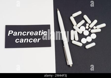 Concetto medico. Su una superficie bianca e nera ci sono pillole, una penna e un segno con l'iscrizione - cancro pancreatico Foto Stock