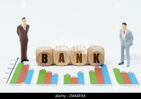 Concetto di business e finanza. Su relazioni finanziarie con grafici, una figura di uomini d'affari e cubi di legno con l'iscrizione - BANCA Foto Stock