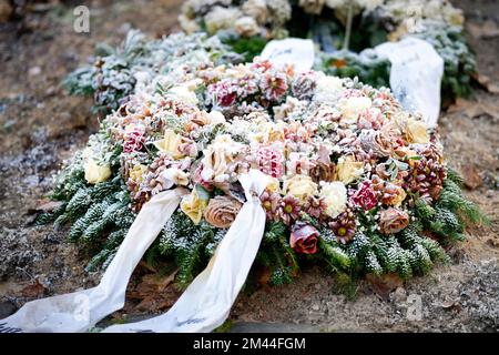 corona funebre con arco e fiori pastello colorati su una tomba coperta di brina Foto Stock