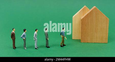 Concetto economico. Sulla superficie verde sono case di legno e figurine in miniatura di persone in piedi in linea per acquistare una casa. Banner Foto Stock