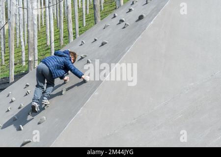 Un ragazzo sale un muro nel parco giochi per bambini all'esterno Foto Stock