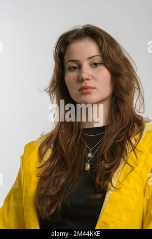 Ritratto di una ragazza vestita di impermeabile giallo che posa e guarda la macchina fotografica isolata su sfondo bianco. Foto Stock