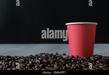 Tazza di carta rossa da asporto. I chicchi di caffè sono sparsi sul tavolo con consistenza. Spazio di copia. orizzontale Foto Stock