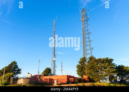 Antenne per telecomunicazioni sulla cima di una collina sotto il cielo limpido al tramonto Foto Stock