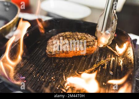 Bistecca alla griglia con fuoco. Gustoso pezzo di bistecca striploin tra fiamme di fuoco poste su padella professionale. Ristorante di carne. Foto di alta qualità Foto Stock