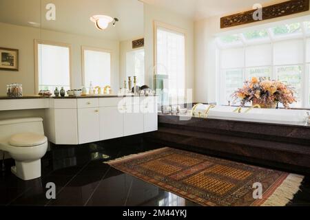 Lavandino laccato bianco e vasca jacuzzi incassata in base di granito in stile marocchino, stanza da bagno principale decorata con tappeto interno casa contemporanea. Foto Stock