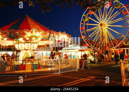 La ruota panoramica e Merry girano le luci di una luce soffusa sotto un cielo crepuscolo Foto Stock