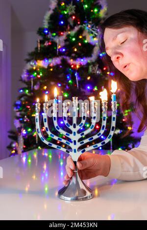 Donna ebrea soffia le candele sul menorah di Hanukkah con nove candele. Foto Stock