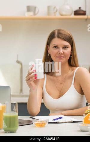 Una giovane donna sta tenendo un vaso bianco di vitamine o pillole. Luogo per il vostro logo Foto Stock