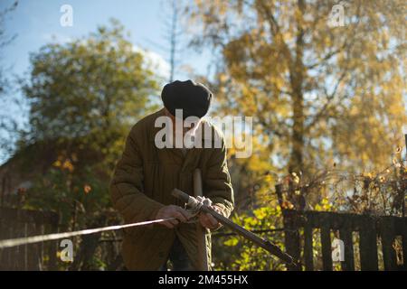 Il vecchio misura la terra. Il nonno tira la corda in giardino. Vecchio che lavora in campagna. In pensione in Russia. Foto Stock