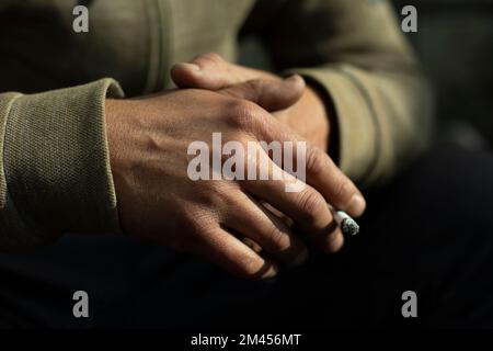 Mano nel dettaglio. Sigaretta inserita tra le confezioni. Luce sul retro della spazzola. Foto Stock