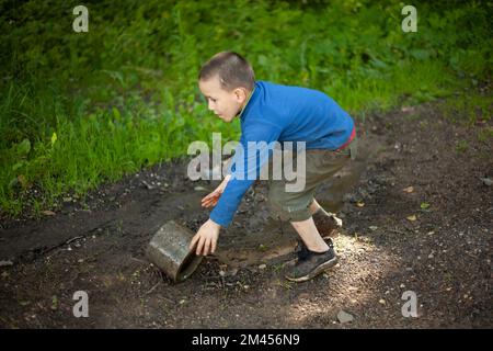 Il bambino tiene un oggetto sporco. Il ragazzino gioca con un anello di cemento. Bambino trovato cosa. L'avventura del bambino in estate. Foto Stock